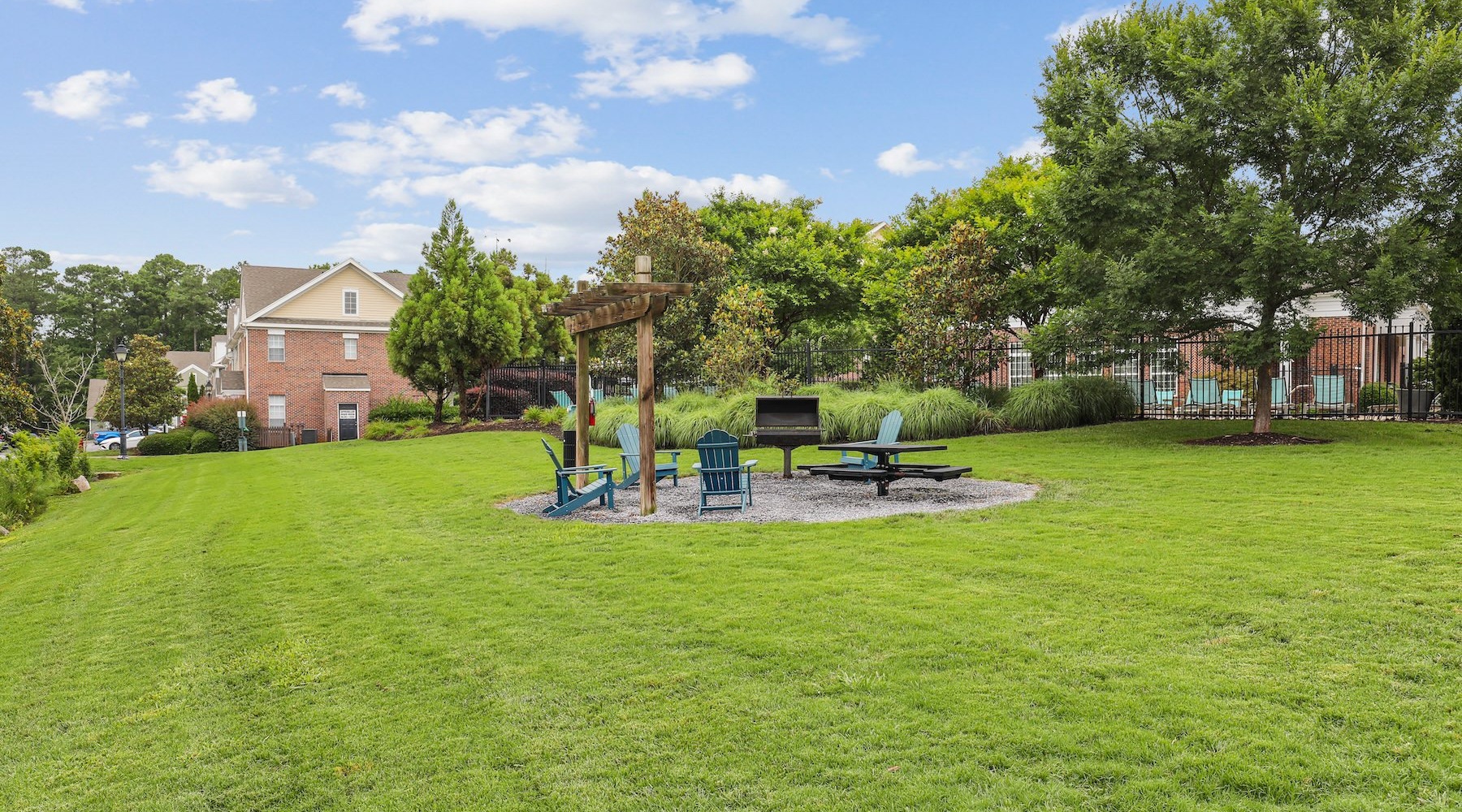 a field of grass and trees with a grill and chairs nearby